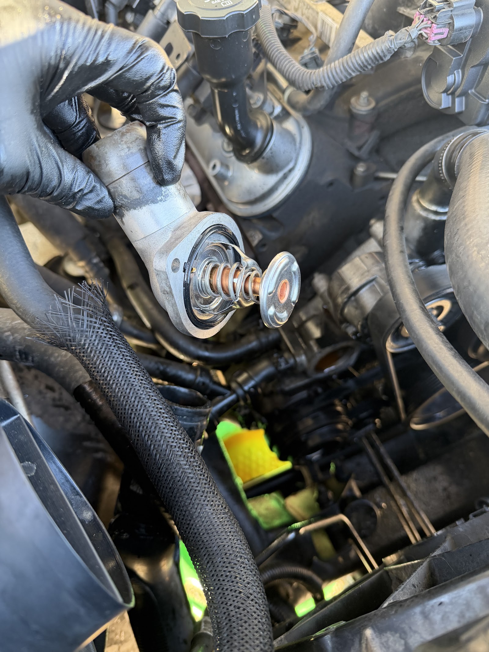 Hand holding a thermostat housing during an engine coolant service