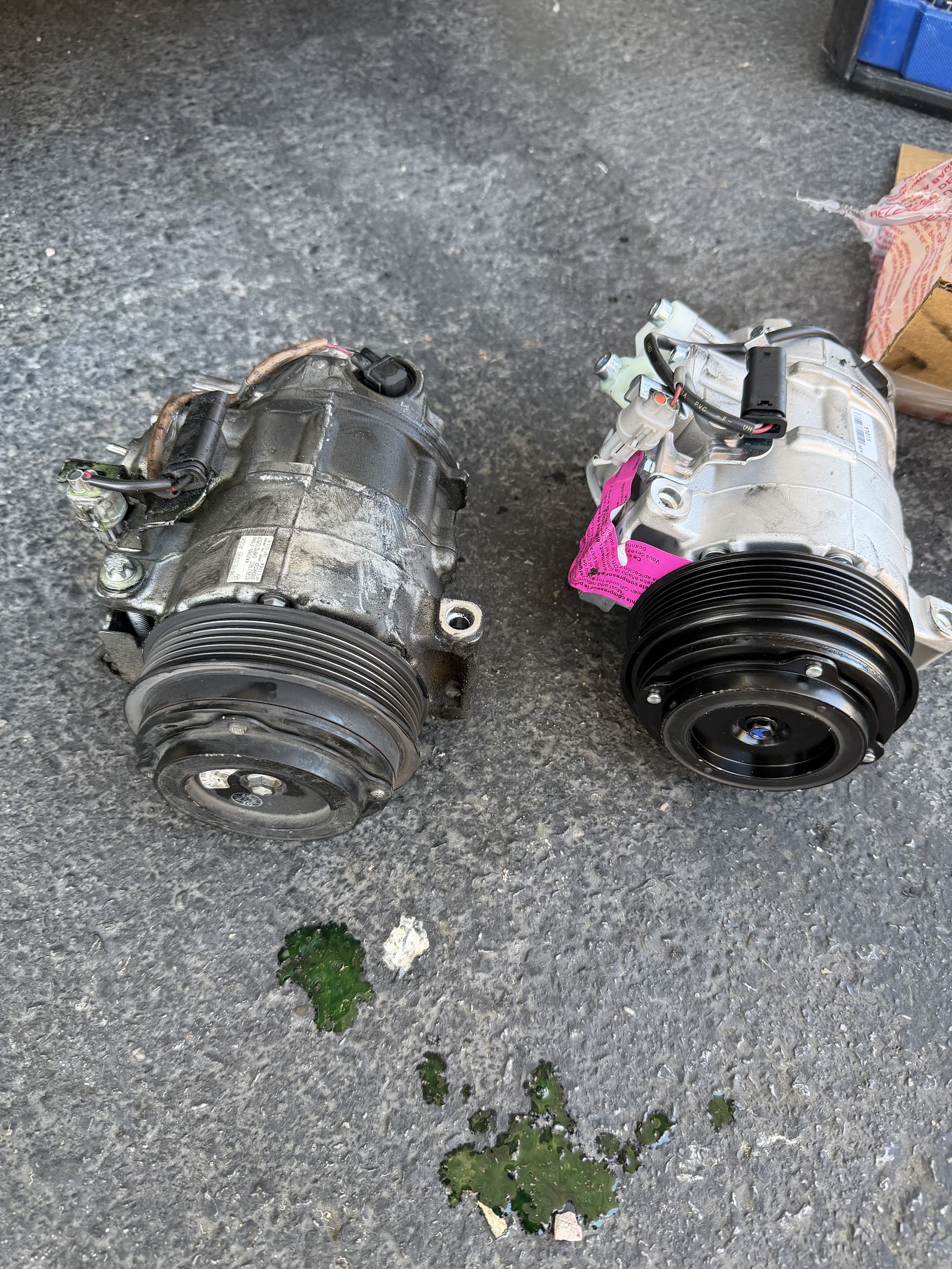 Old and new AC compressors side by side on pavement