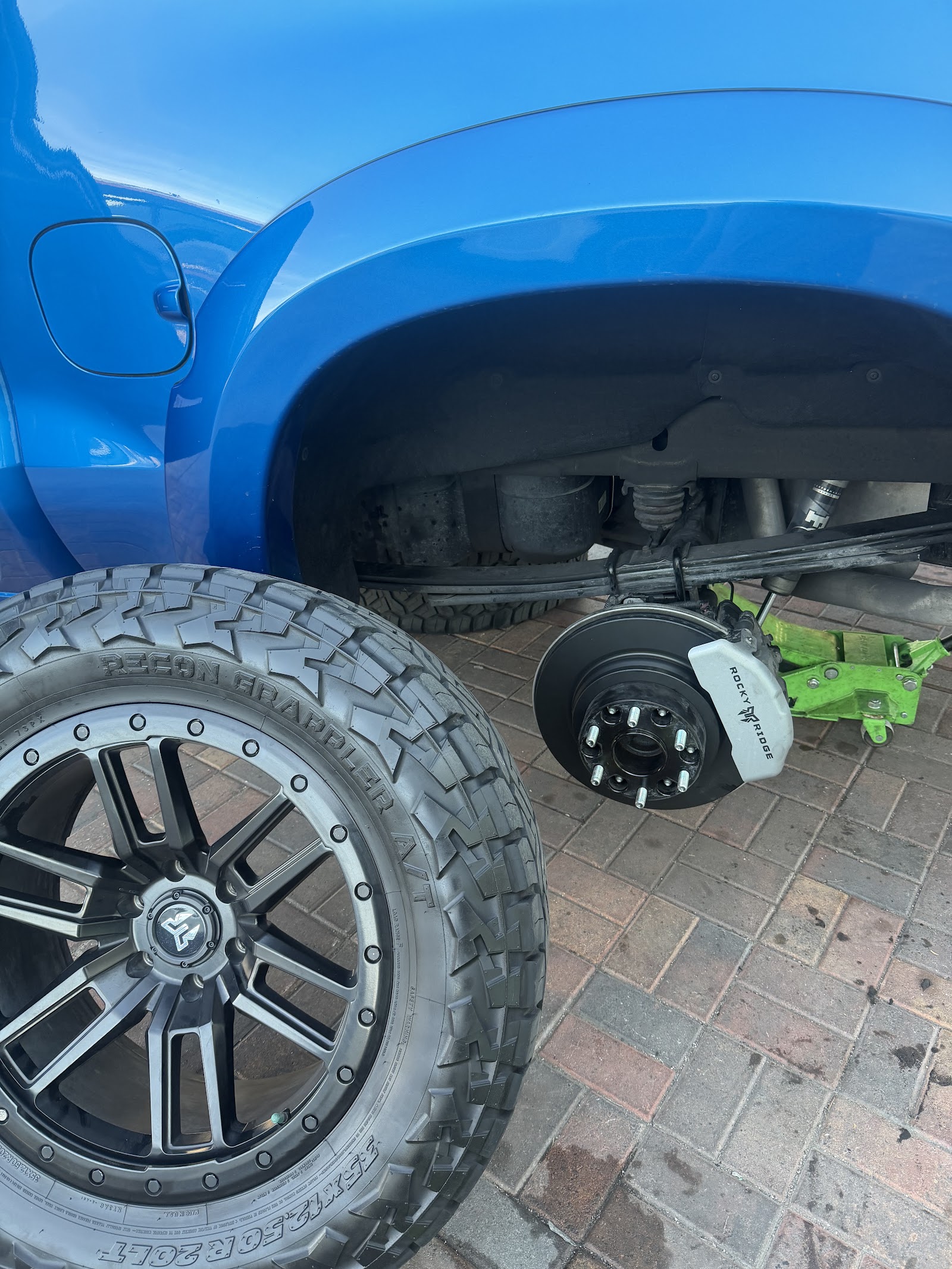 Lifted blue truck raised on a jack with Rocky Ridge brakes and an aftermarket wheel removed